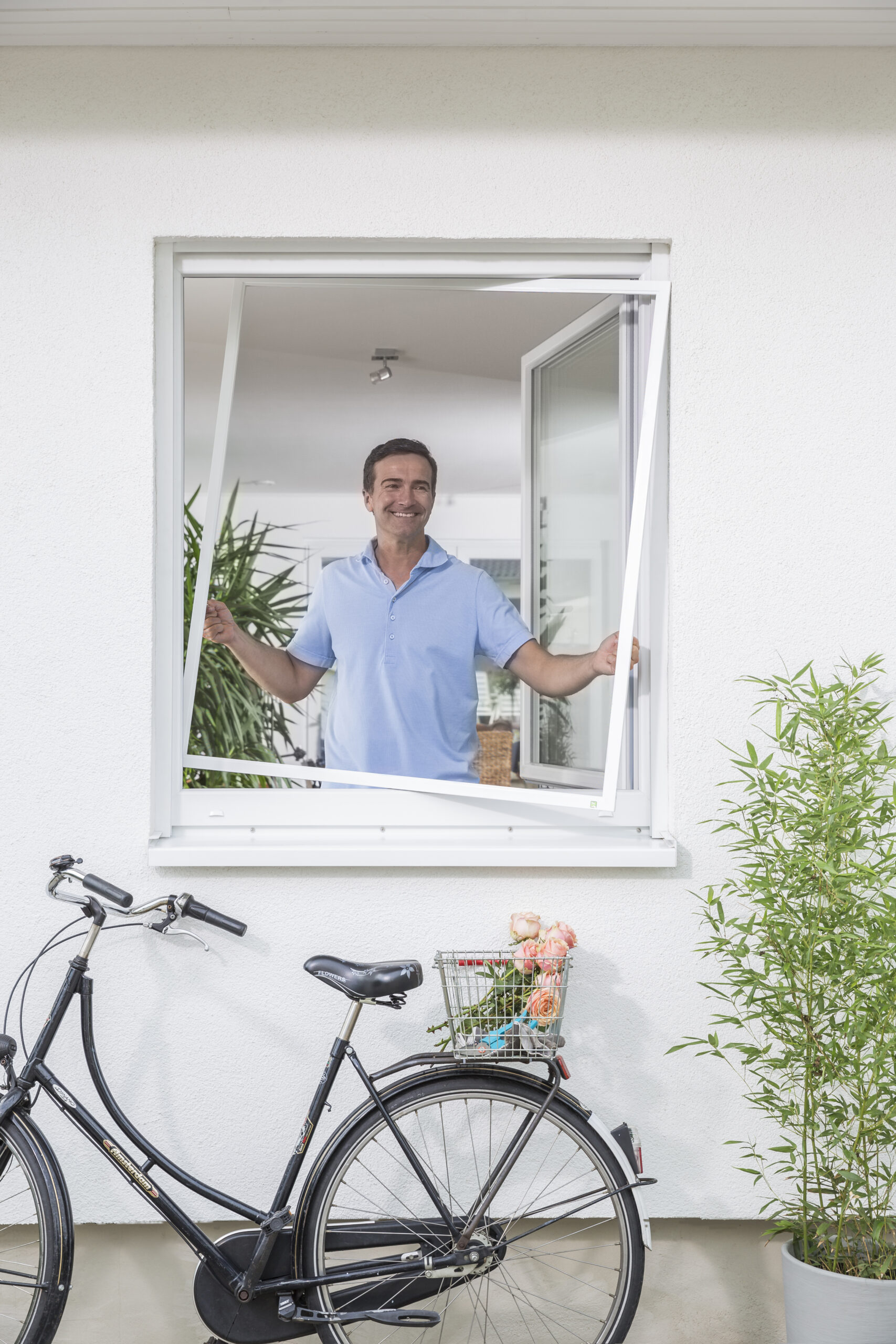 Mann öffnet Fenster mit installiertem Fliegengitter Spannrahmen einflügelig