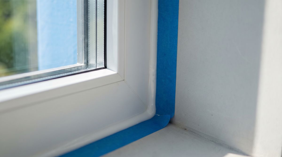 Nahaufnahme einer frisch aufgetragenen Silikonfuge zwischen Fensterrahmen und Wand